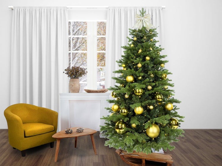 Geschmückter künstlicher Weihnachtsbaum mit goldenen Kugeln und Sternspitze in einem Wohnzimmer mit Sessel und kleinem Holztisch.