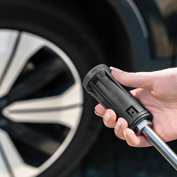 Eine Hand hält eine schwarze Hochdruckreiniger-Düse mit verstellbarem Sprühbild vor einer Autofelge.