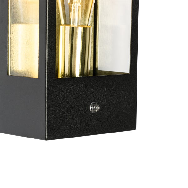 Nahaufnahme einer modernen schwarzen Außenwandleuchte mit Glaseinsätzen, goldfarbener Fassung und integriertem Dämmerungssensor.