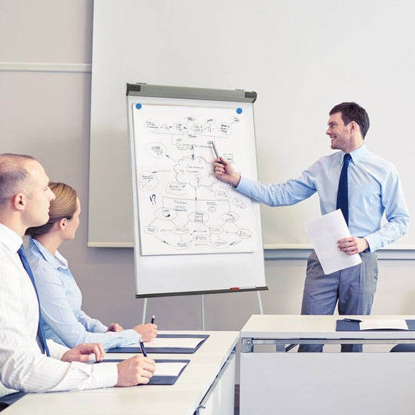 Präsentation an einem Flipchart mit Diagramm in einem hellen, organisierten Büro mit Kollegen.