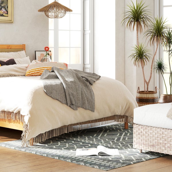 Helles Schlafzimmer mit Holzbett, Fransen-Tagesdecke, gemustertem Teppich, geflochtener Pendelleuchte und Zimmerpflanzen. Natürlicher, luftiger Stil.