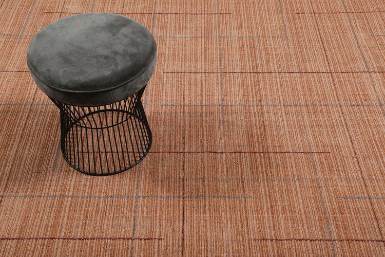 Moderner Teppich mit linearem Muster und Karos, darauf ein Hocker mit Samtpolster und Drahtgestell.
