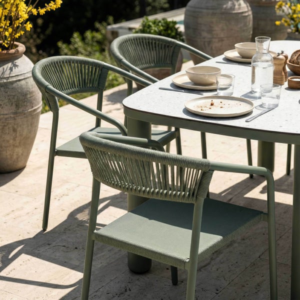 Moderne Garten-Essgruppe mit grünen Seilgeflecht-Stühlen und einem Tisch mit Steinoptik-Platte auf einer hellen Terrasse.