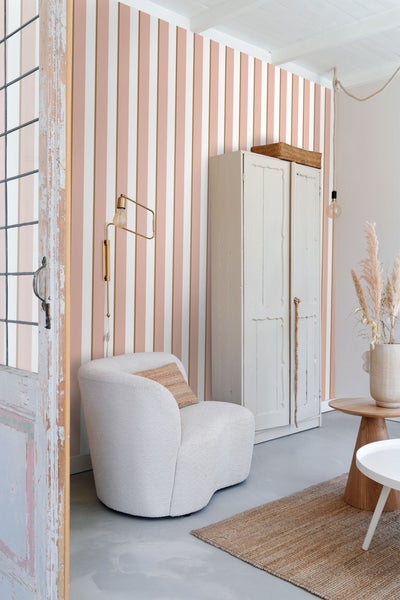 Wohnzimmer mit gestreifter Tapete, Sessel und Schrank für eine helle und organisierte Atmosphäre.