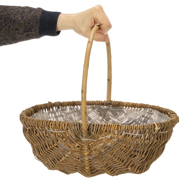 Ovaler Weidenkorb mit hohem Henkel und Folienauskleidung, von einer Hand gehalten.