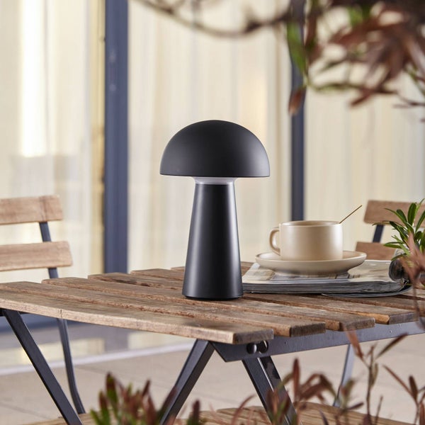 Pilzförmige LED-Tischleuchte auf einem hölzernen Gartentisch im Außenbereich mit einer Kaffeetasse.