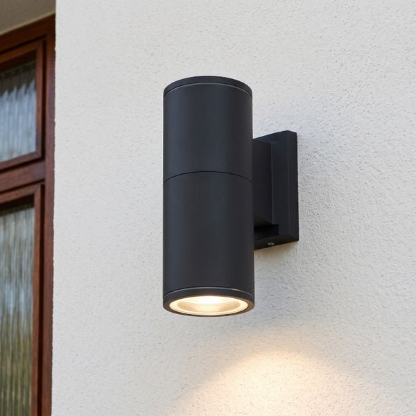 Moderne zylindrische LED Außenwandleuchte für den Fassadeneinsatz mit nach unten gerichtetem Lichtaustritt an einer weißen Hauswand