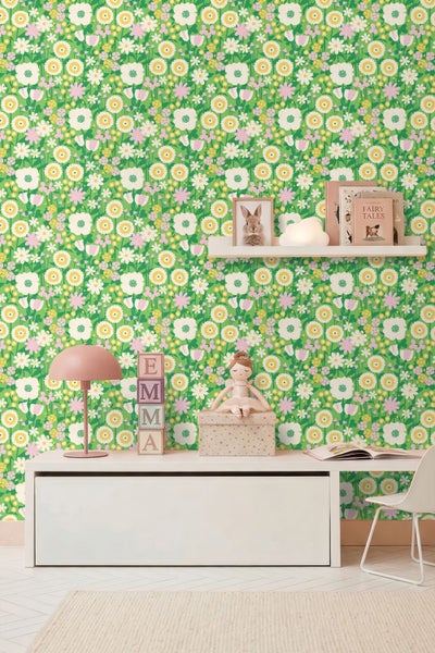 Hell gestaltetes Kinderzimmer mit Vliestapete in floralem Muster, weißer Sitzbank, Schreibtischlampe und Wandregal mit Dekoration.