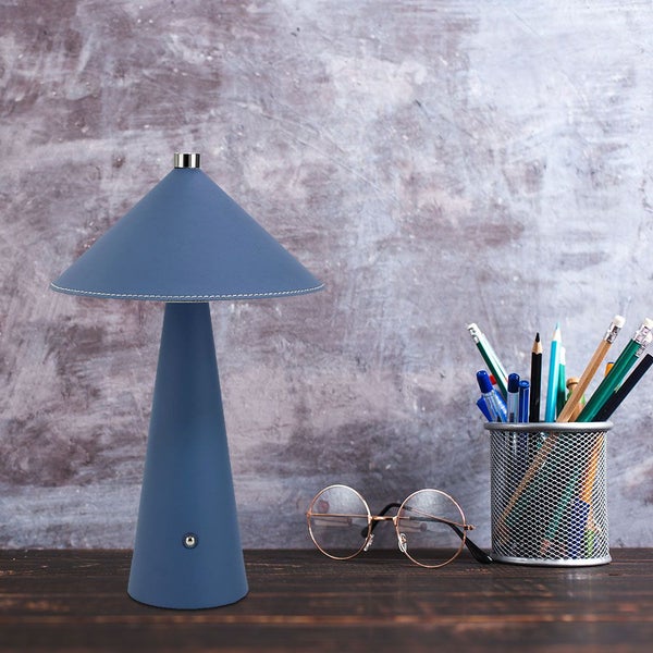 Blaue Tischleuchte mit konischem Schirm auf einem Schreibtisch mit Stiften und Brille