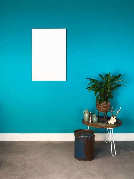 Moderne Raumgestaltung mit blauer Wand, weißem Bilderrahmen, Holzbeistelltisch mit Zimmerpflanze und Betonboden.