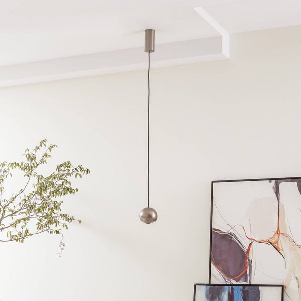Minimalistische Pendelleuchte aus gebürstetem Metall mit kleinem kugelförmigem Schirm und schwarzem Kabel in einem hellen, modernen Raum.