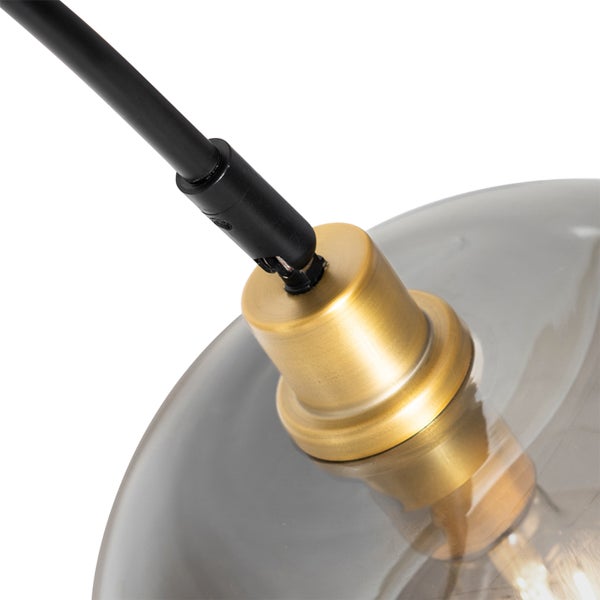 Detail einer modernen Leuchte mit schwarzem Metallstab, messingfarbener Halterung und rauchgrauem Glasschirm.