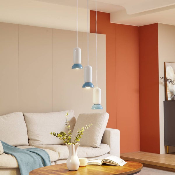 Modernes Wohnzimmer mit beigem Sofa und Holztisch. Drei weiß-blaue Pendelleuchten hängen in verschiedenen Höhen und schaffen eine helle Atmosphäre.