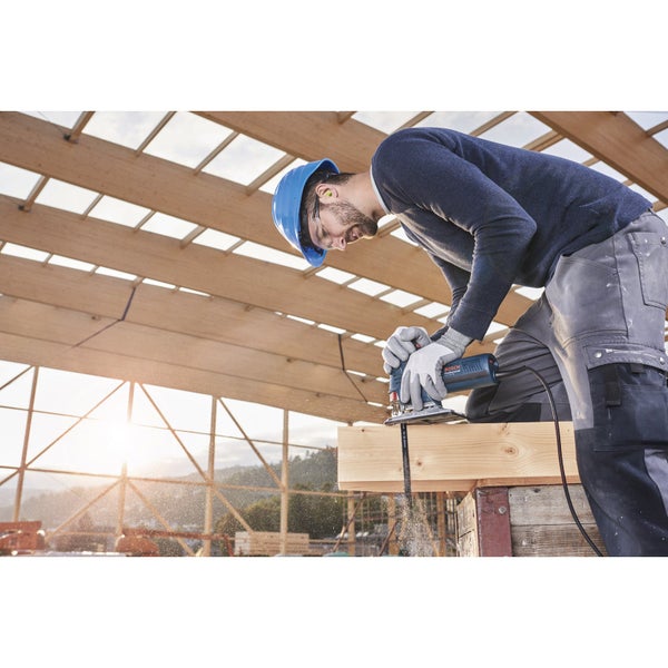 Ein Handwerker sägt mit einer Stichsäge ein Holzbrett. Er trägt einen Helm und Handschuhe.