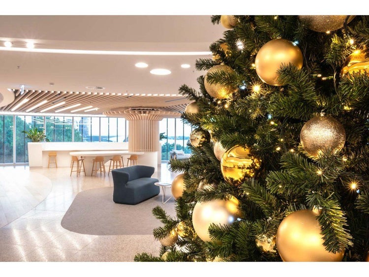 Weihnachtsbaum geschmückt mit Kugeln in einem modernen, hellen Büro-Empfangsbereich mit Lounge-Möbeln und Holzstrukturen.