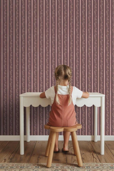 Gestreifte Tapete mit floralem Muster in einem Kinderzimmer. Ein Kind sitzt an einem weißen Schreibtisch vor der verzierten Wand.
