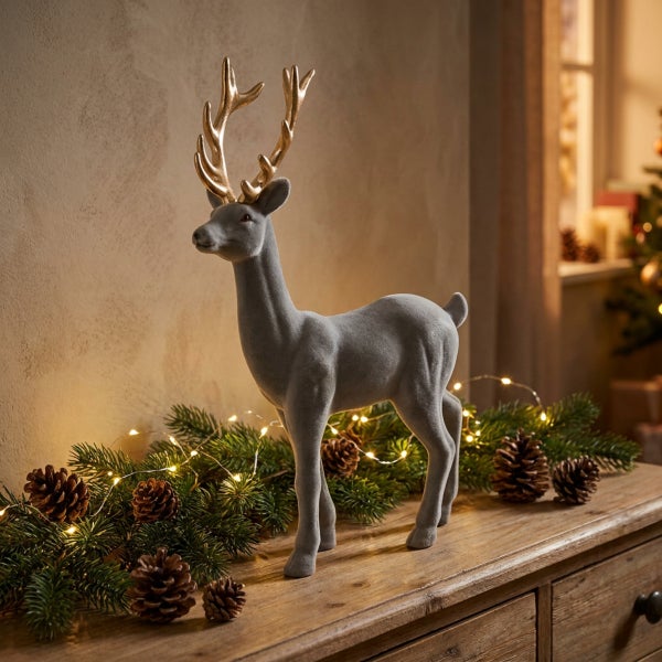 Dekorative Weihnachtsfigur in Form eines Rentiers mit goldenem Geweih, auf einem hölzernen Sideboard dekoriert mit Tannenzweigen und Lichterkette.
