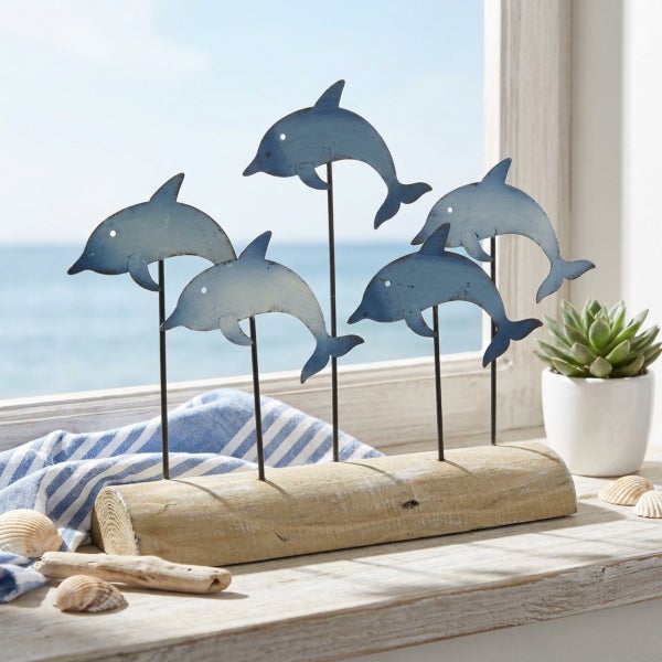 Dekoaufsteller mit vier Delfinfiguren aus Metall auf einem naturbelassenen Holzsockel zur maritimen Dekoration.