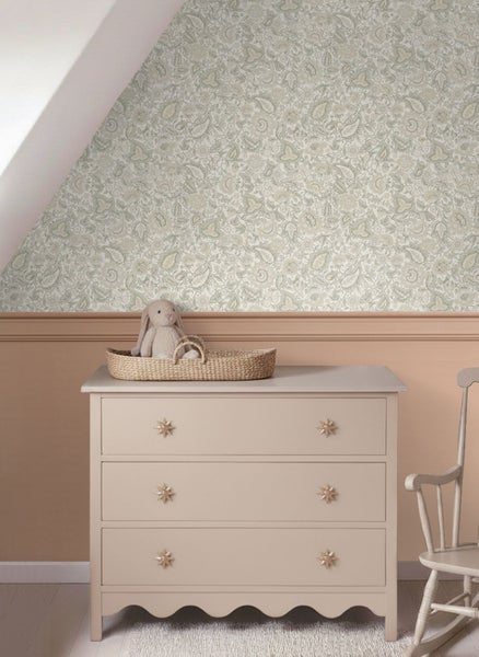 Kinderzimmerwand mit floral gemusterter Tapete und Wandpaneelen, Holzkommode mit sternförmigen Griffen und ein Schaukelstuhl.