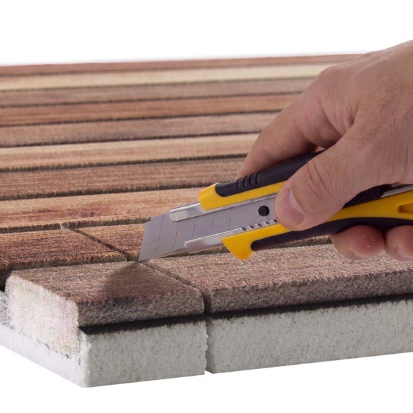 Hand schneidet mit einem Cuttermesser eine Isolierplatte mit Holzoptik Oberfläche zu.