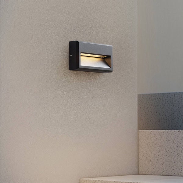Moderne rechteckige Wandleuchte an einer strukturierten Wand über einer Treppe, die warmes Licht nach unten auf die Stufen wirft.