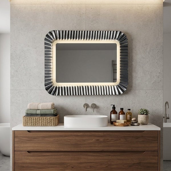 Moderner Badezimmerspiegel mit LED-Beleuchtung und geriffeltem Rahmen über einem Waschtisch aus Holz mit weißem Aufsatzbecken vor einer Steinwand.