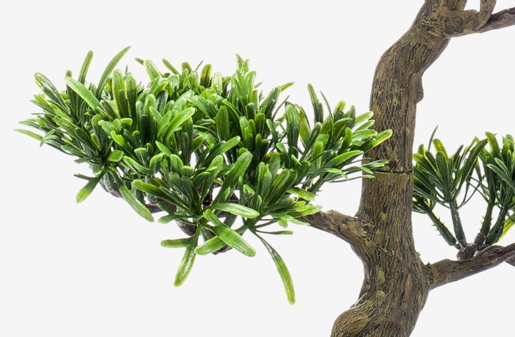 Basis eines künstlichen Bonsais in einer dunklen ovalen Schale mit dekorativen Kieselsteinen auf der Oberfläche.