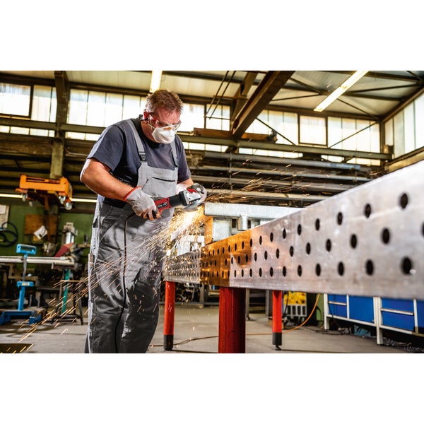 Handwerker bearbeitet ein Metallteil mit einem Winkelschleifer in einer Werkstatt und trägt dabei Schutzkleidung und Schutzbrille.