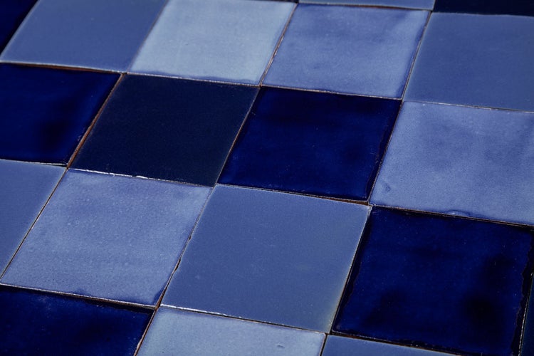 Nahaufnahme von quadratischen, keramischen Fliesen in verschiedenen Blaunuancen.