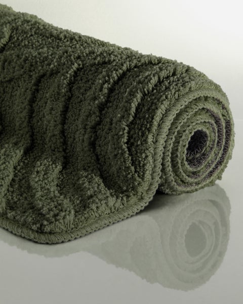 Zusammengerollte Badematte in Grün mit Hochflor-Struktur.