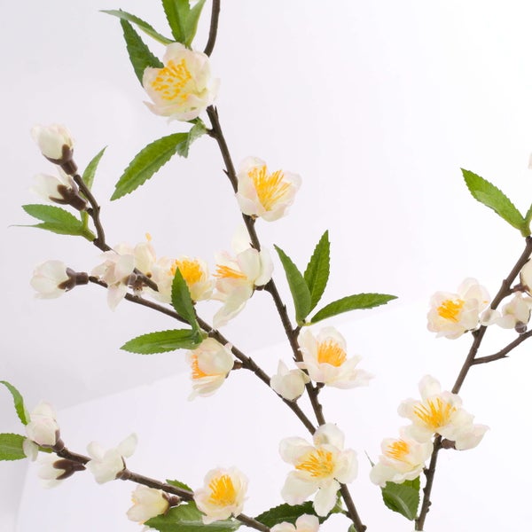Künstlicher Blütenzweig mit weißen Blüten und grünen Blättern.