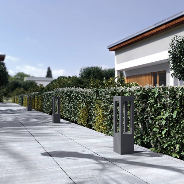 Moderne quadratische Pollerleuchten aus Metall in Anthrazit an einem gepflasterten Gartenweg neben einer grünen Hecke im Außenbereich.