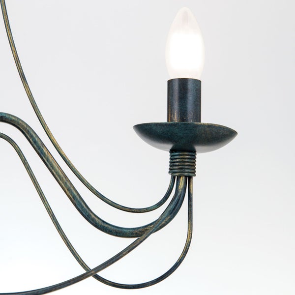 Detailansicht eines rustikalen Kronleuchters aus Metall mit geschwungenen Armen und einer brennenden Kerzenlampe.