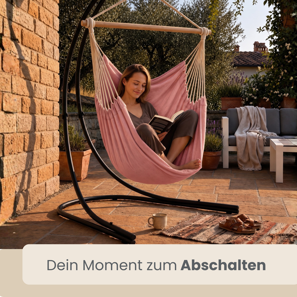 Frau liest Buch in einem Hängesessel mit Metallgestell auf einer Terrasse.