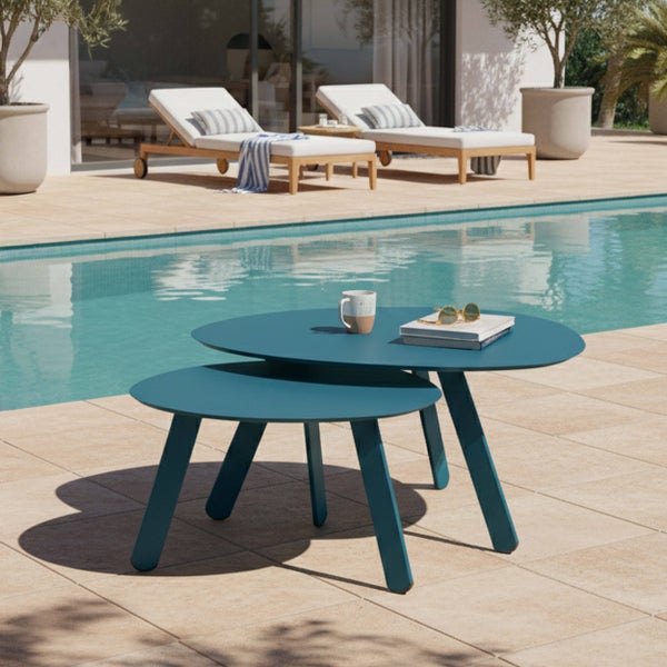 Moderne Satztische für den Außenbereich in Blau auf einer gefliesten Terrasse neben einem Pool, mit Sonnenliegen und Pflanzen im Hintergrund.