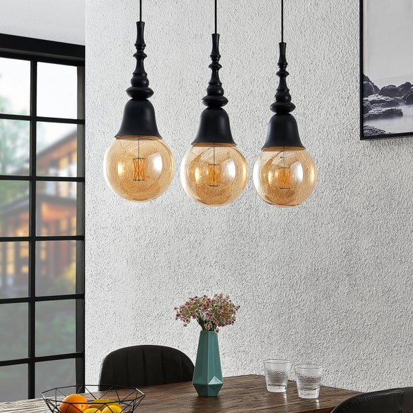 Drei Pendelleuchten mit schwarzen Fassungen und bernsteinfarbenen Glühbirnen über einem Esstisch.