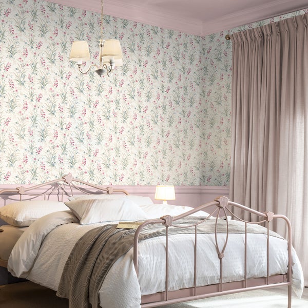 Schlafzimmer mit romantischer Blumentapete, Metallbett und Vorhängen in einer harmonisch gestalteten Einrichtung.
