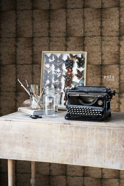 Dekorative Szene mit einer alten Schreibmaschine, einem Schmetterlingsrahmen und Vintage-Elementen auf einem Holztisch vor einer Wand mit Kachelmuster.