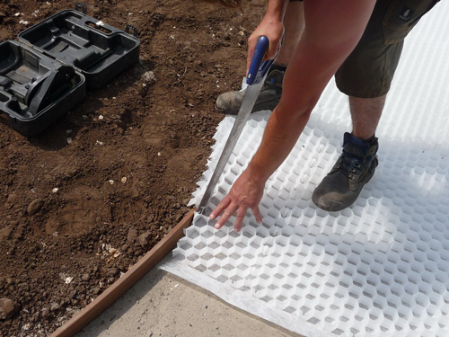 Eine Person schneidet eine weiße Kieswabe aus Kunststoff mit einer Handsäge auf einer Baustelle zu.