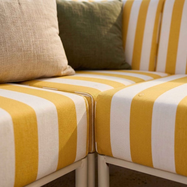 Detailansicht eines Loungesofas mit gelb-weiß gestreiften Polstern sowie einem beigen und einem olivgrünen Kissen.