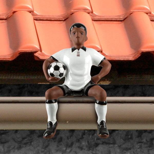 Dachschmuck Firstfigur Fußballer aus Keramik, sitzend mit Fußball, in weiß-schwarzer Sportkleidung auf einem Hausdach.