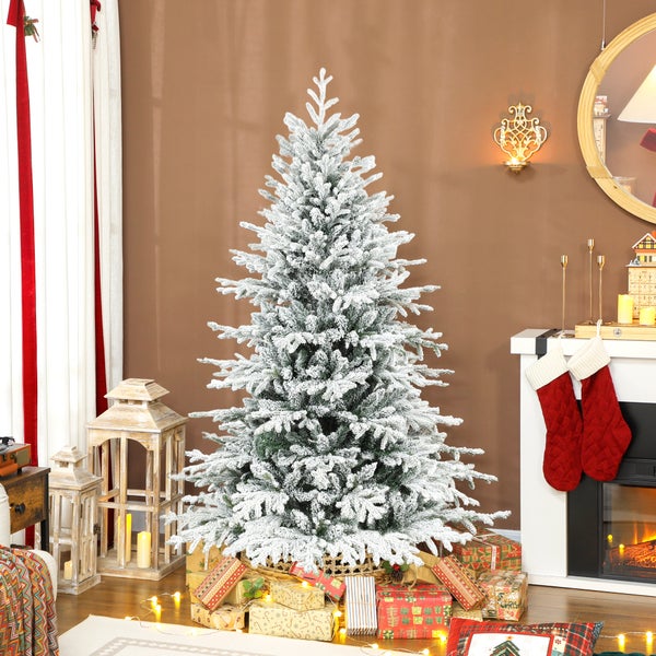 Künstlicher Weihnachtsbaum mit Schneeeffekt in einem festlich dekorierten hellen Raum mit Kamin, Holzlaternen und Geschenken.