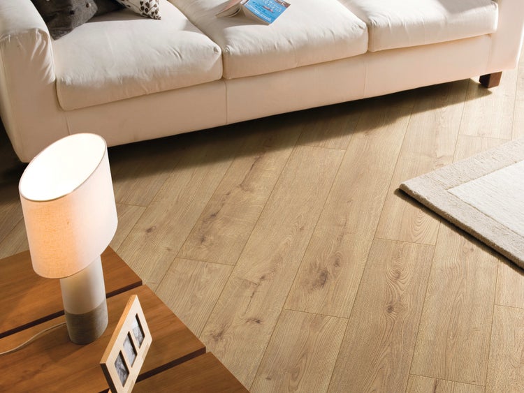 Helles Laminat in Holzoptik in einem Wohnzimmer mit Sofa und Stehlampe.