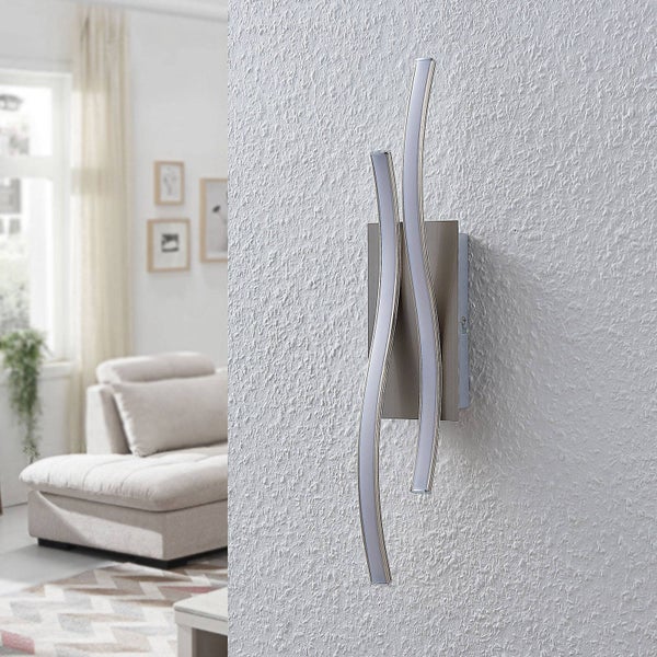 Moderne Wandleuchte mit zwei geschwungenen Lichtelementen und Metallsockel an einer strukturierten Wand in einem hellen Wohnzimmer.
