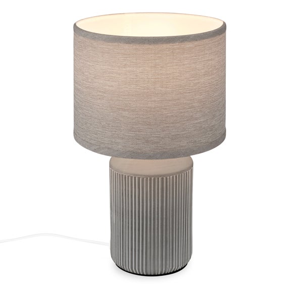 Tischleuchte mit grauem Textilschirm und geripptem Keramikfuß.