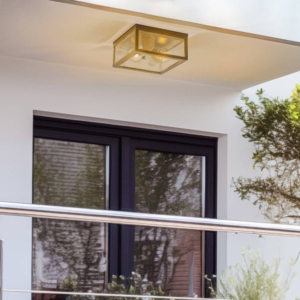 Quadratische Außen-Deckenleuchte mit Messingrahmen und Glasscheiben, montiert an einer Decke im Außenbereich über einem Fenster.