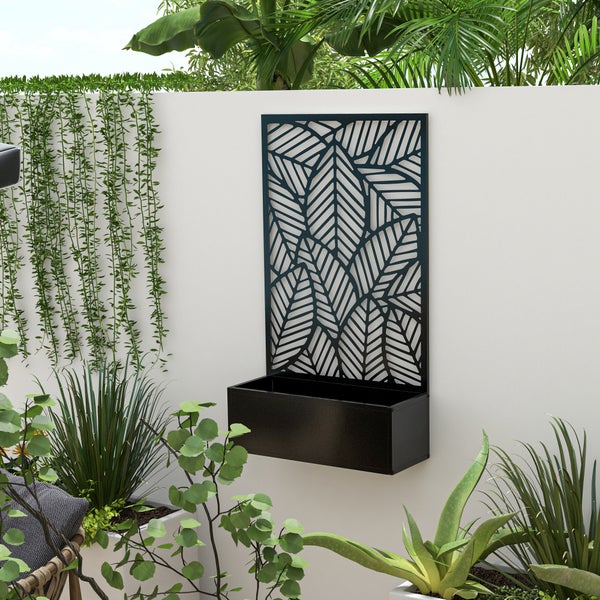 Schwarzer Pflanzkasten aus Metall mit Sichtschutz im Blatt-Design auf einer Terrasse neben einer Gartenbank.