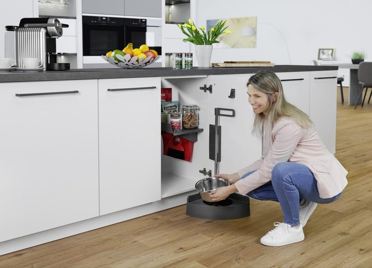 Frau nutzt ein Ordnungssystem für Haustierzubehör in einem Küchenunterschrank mit Futternapf und Ablagen in einer modernen, hellen Küche.
