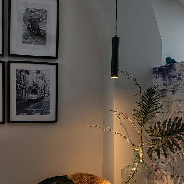 Zimmeransicht mit einer Pendelleuchte, Fotos an der Wand und einer Pflanze in einer Glasvase