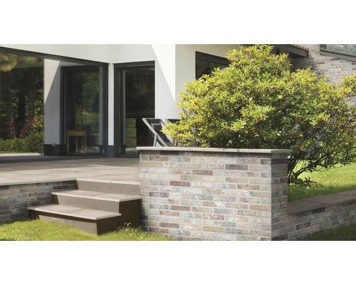 Moderne Terrasse mit einer niedrigen Stützmauer aus Riemchen in Ziegeloptik und einer Treppe mit Blockstufen vor einem modernen Wohnhaus.